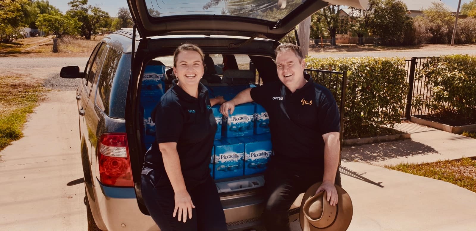 Woman and man stand beside car boot filled with boxes of water
