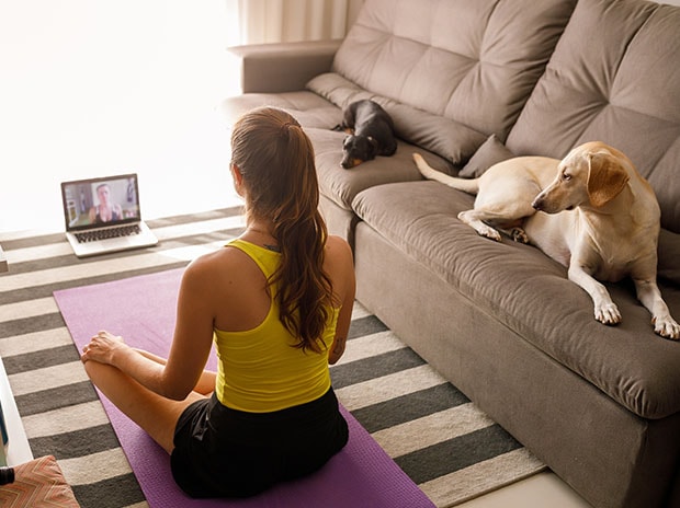 Lady in fitness atire sitting on a yoga mat watching an online workout on a laptop