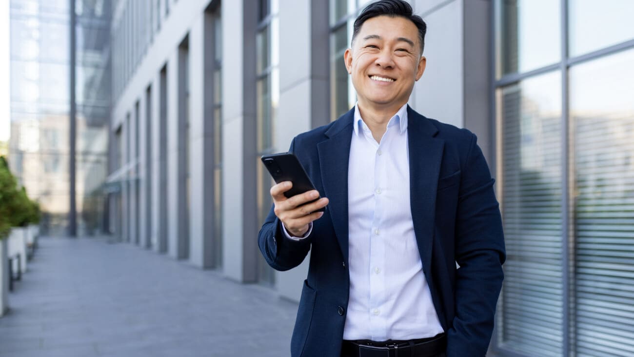 Young businessman in a suit smiling while holding a mobile phone.