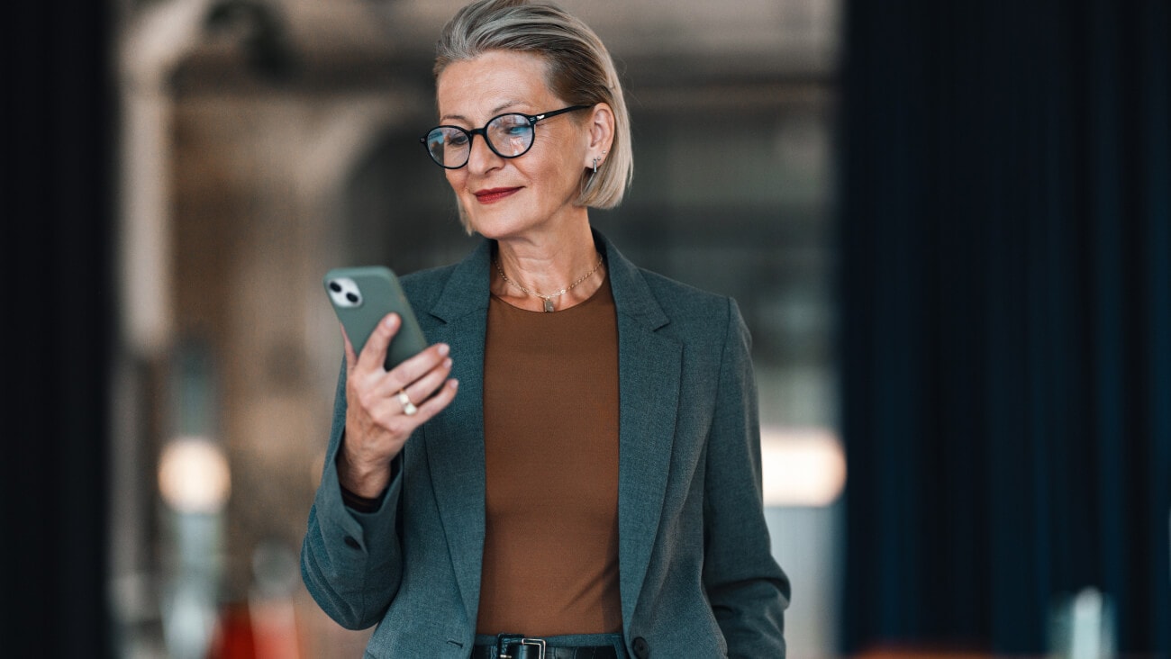 Business woman in a suit wearing glasses looking at the mobile phone in her hand
