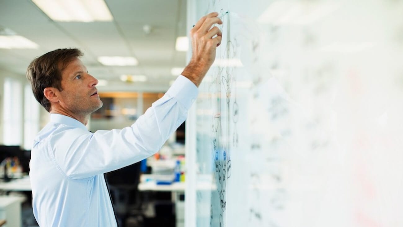 Business man standing at a whiteboard working out the pros and cons of expanding the business.