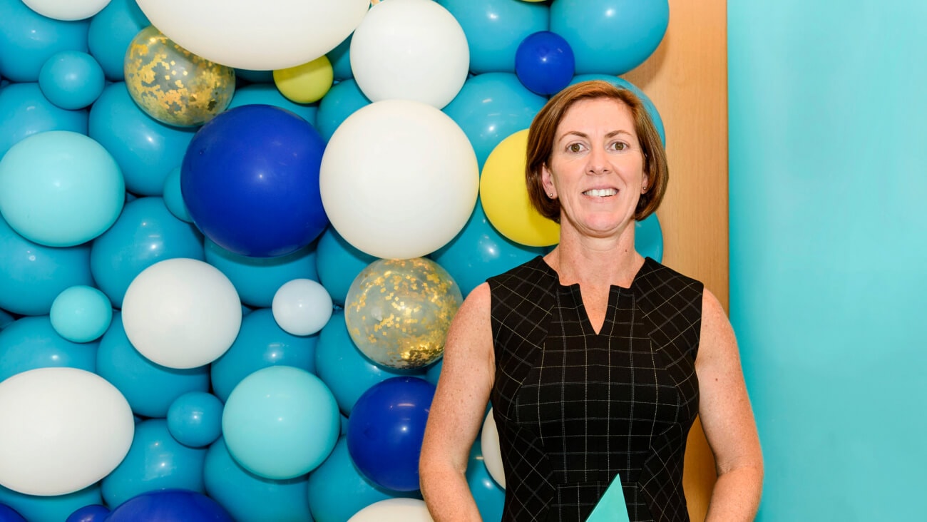Dervla Loughnane, Founder of Virtual Psychologist, standing in front of a colourful background made up of blue and white balloons.
