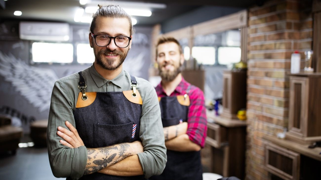 Two smiling men wearing work aprons.