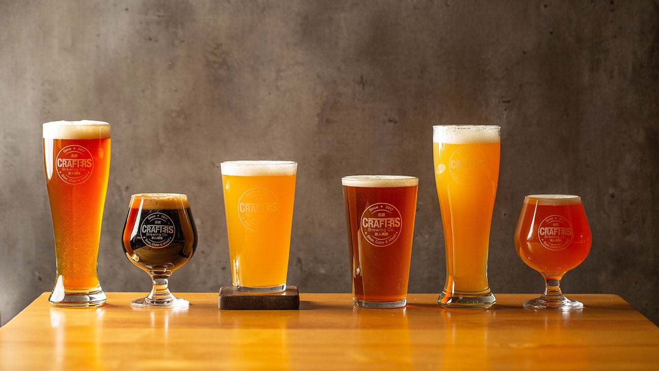 six different types of beers in a line on a table with grey background