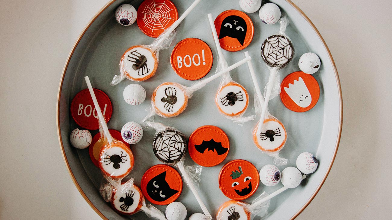 Bowl of Halloween candy with spider lollypops, edible eyeballs and chocolates with bats, vats and boo symbols printed on them.
