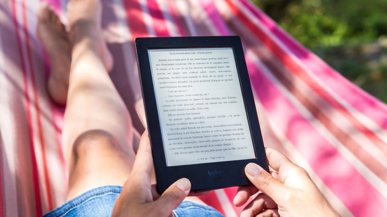 Woman reading an Amazon Kindle while sitting on a picnic rug