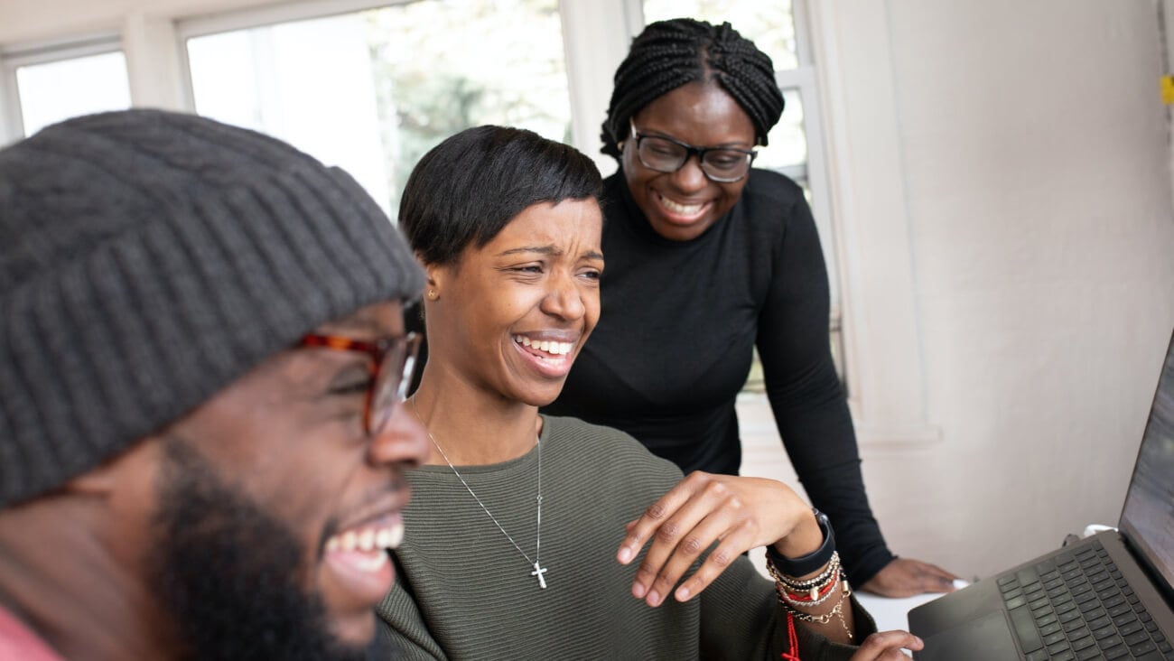 three people laughing while watching a movie on a laptop computer