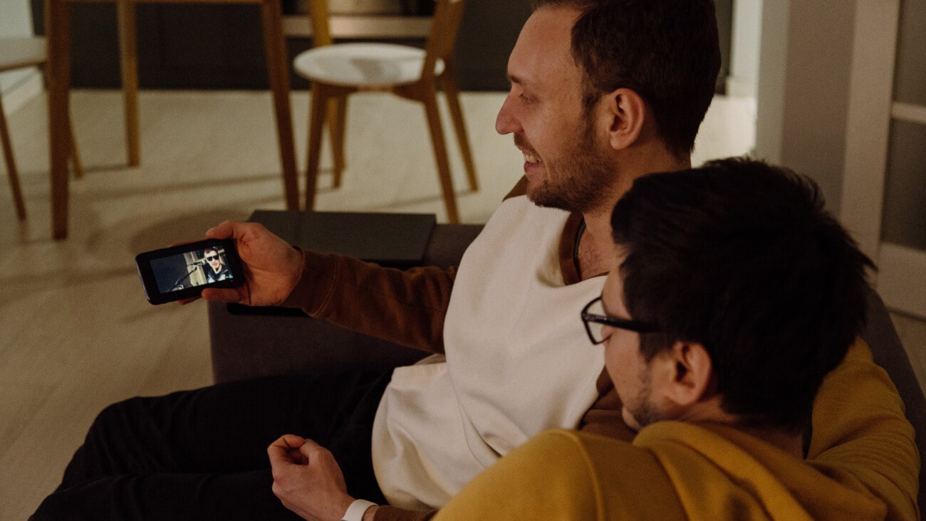 two men sitting on couch watching something on phone