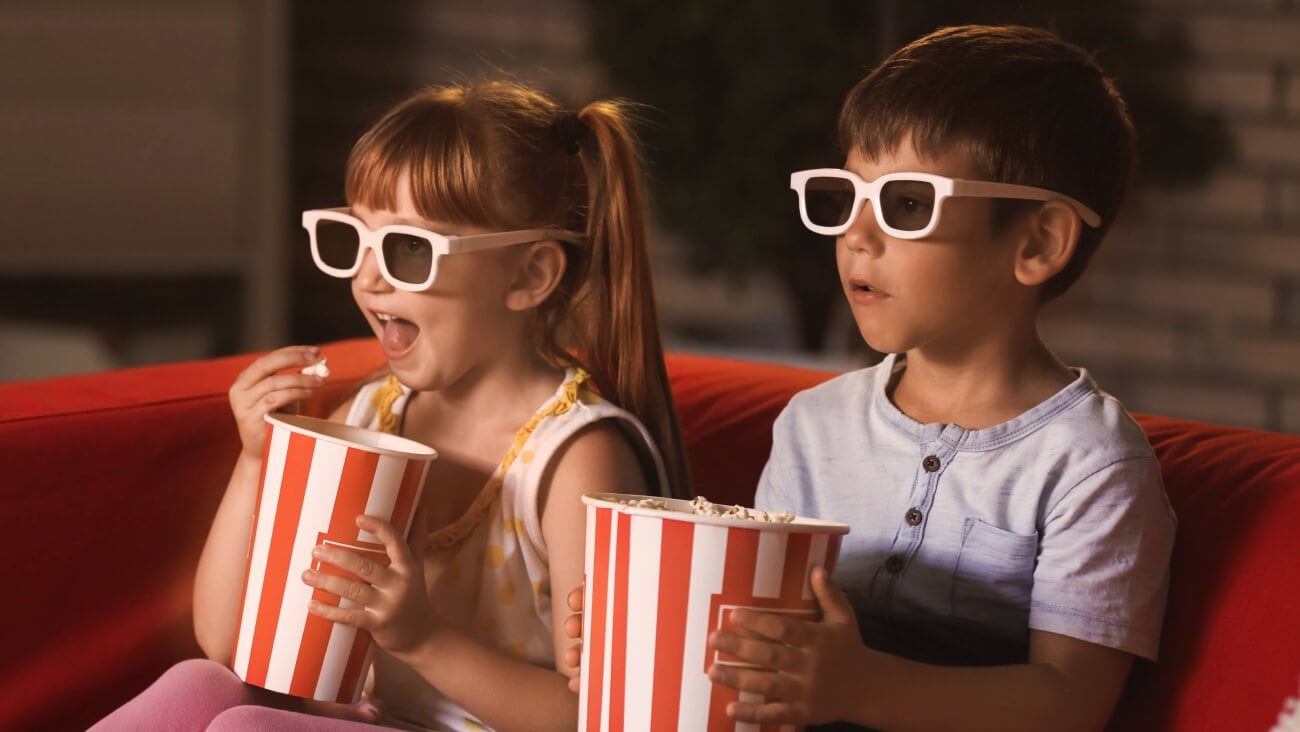 Young girl and boy watching a movie while eating popcorn at home.