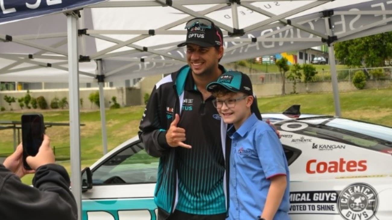 Chaz Mostert and a student from Toogoolawa School, Queensland standing in front of the Mobil 1 Optus Racing car during the 2024 Gold Coast 500.