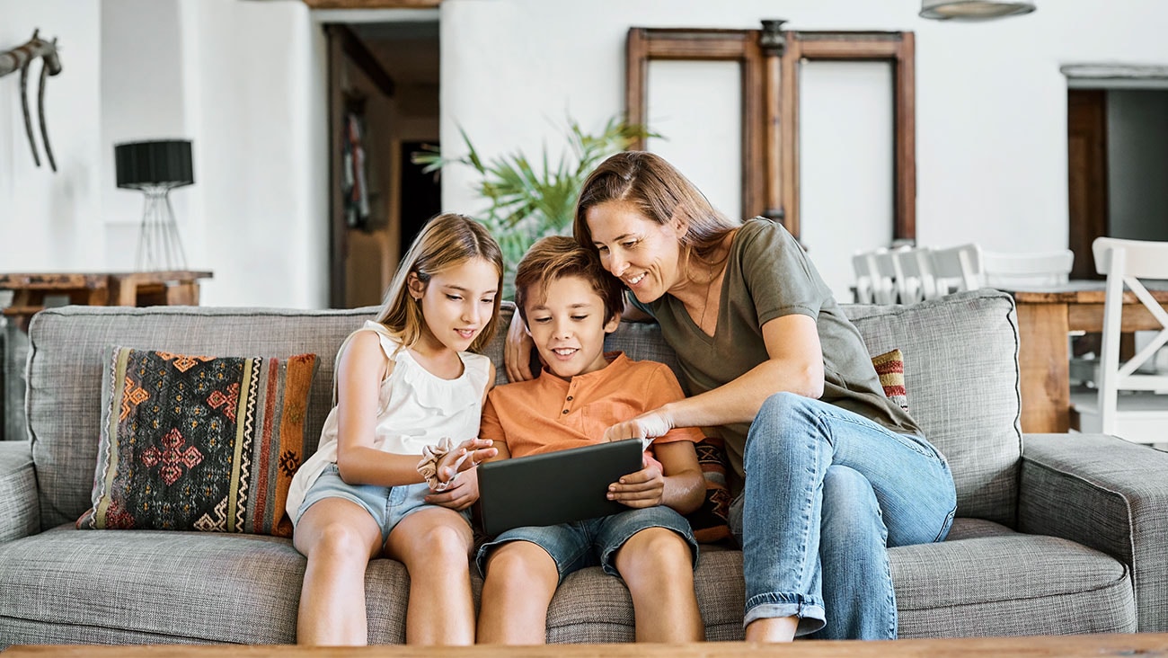 teenage girl, younger boy holding a tablet and mum sitting on a sofa