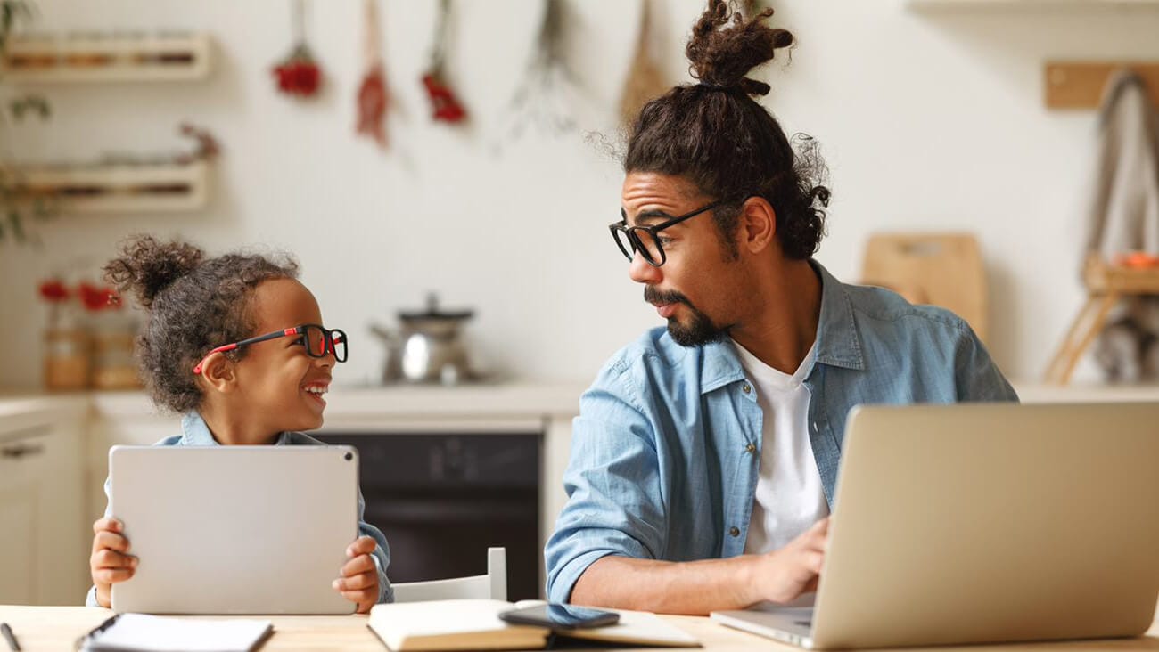 Father and daughter using devices while looking at each other smiling.