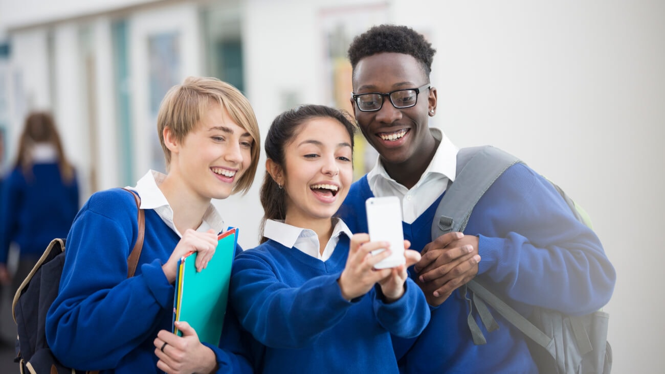 Three students looking at a mobile phone while being aware of the importance of cybersafety and how to combat cyberbullying.