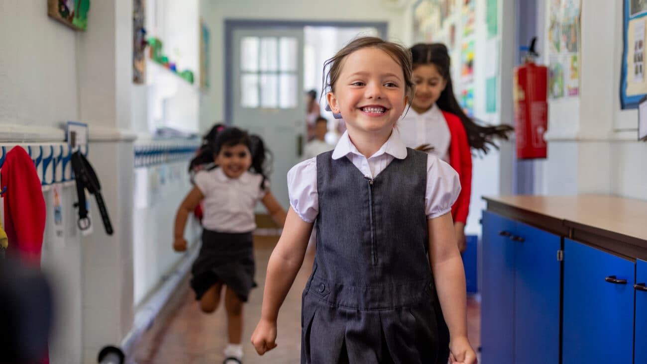 Young schoolgirl in uniform running through school corridor smiling