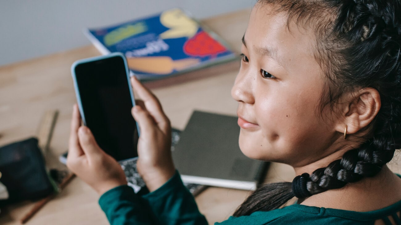 Young girl holding a mobile phone sitting at a desk with books
