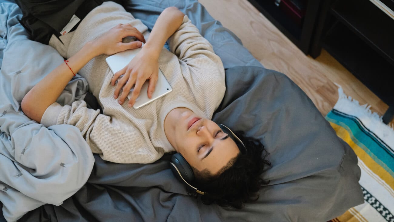 Young guy is relaxing on his bed wearing headphones