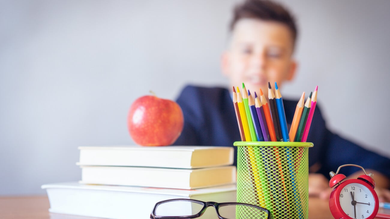Boy in school uniform with books, pencils, glasses, clock and an apple.