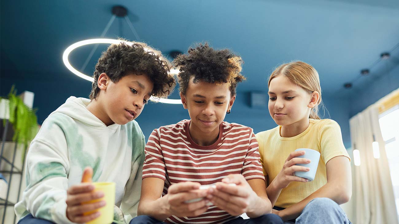 three diverse tweens, 2 boys and girl looking at a mobile phone