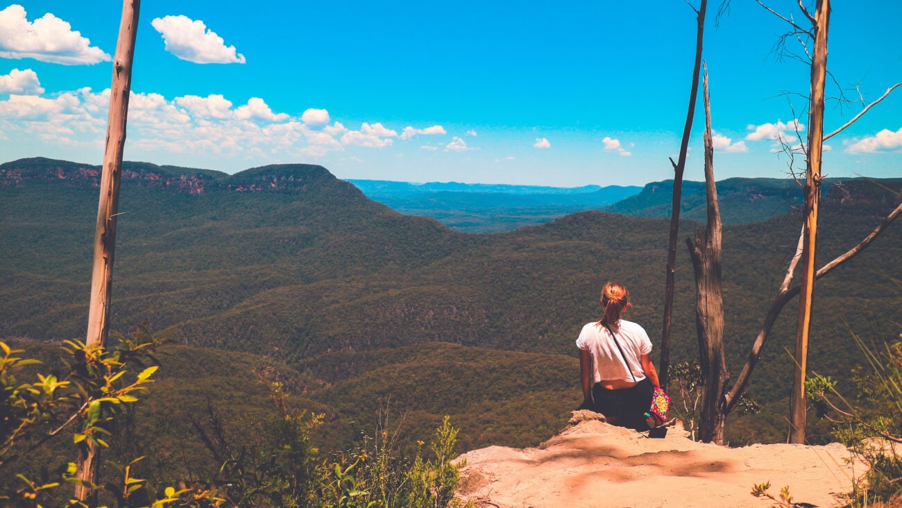 Woman sits on the edge of a cliff and looks out over the Blue Mountains