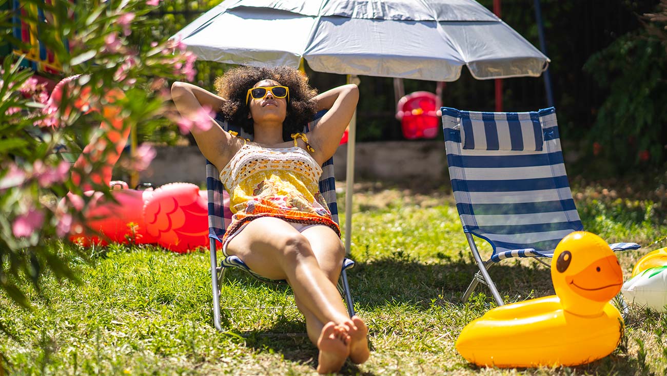 Young woman sun bathing in the back yard surrounded by pool toys with a beach umbrella.