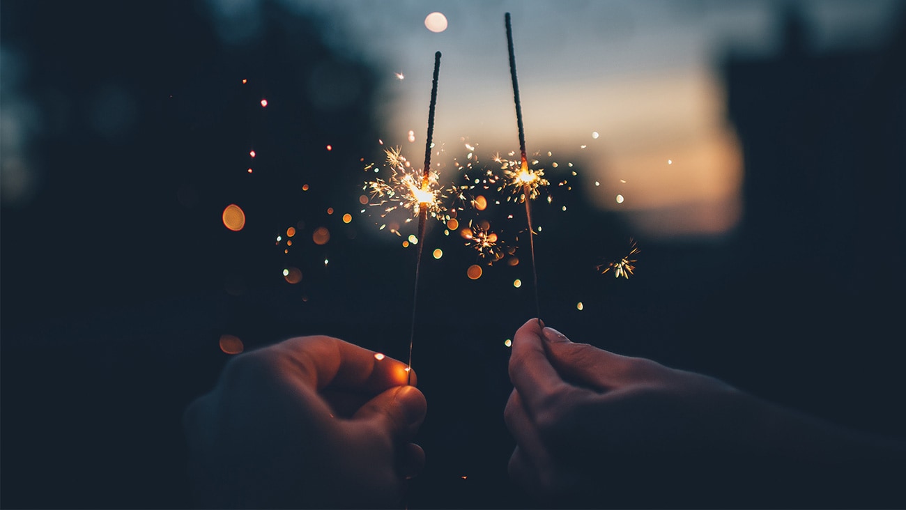 two people holding sparklers against the night sky