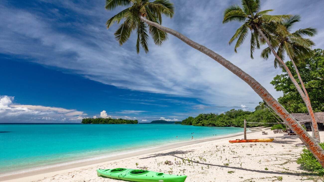 Beach scene in Vanuatu with a kayak on the sand and palm trees.
