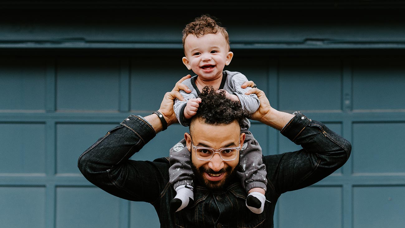 A father holding his baby son on his shoulders and smiling