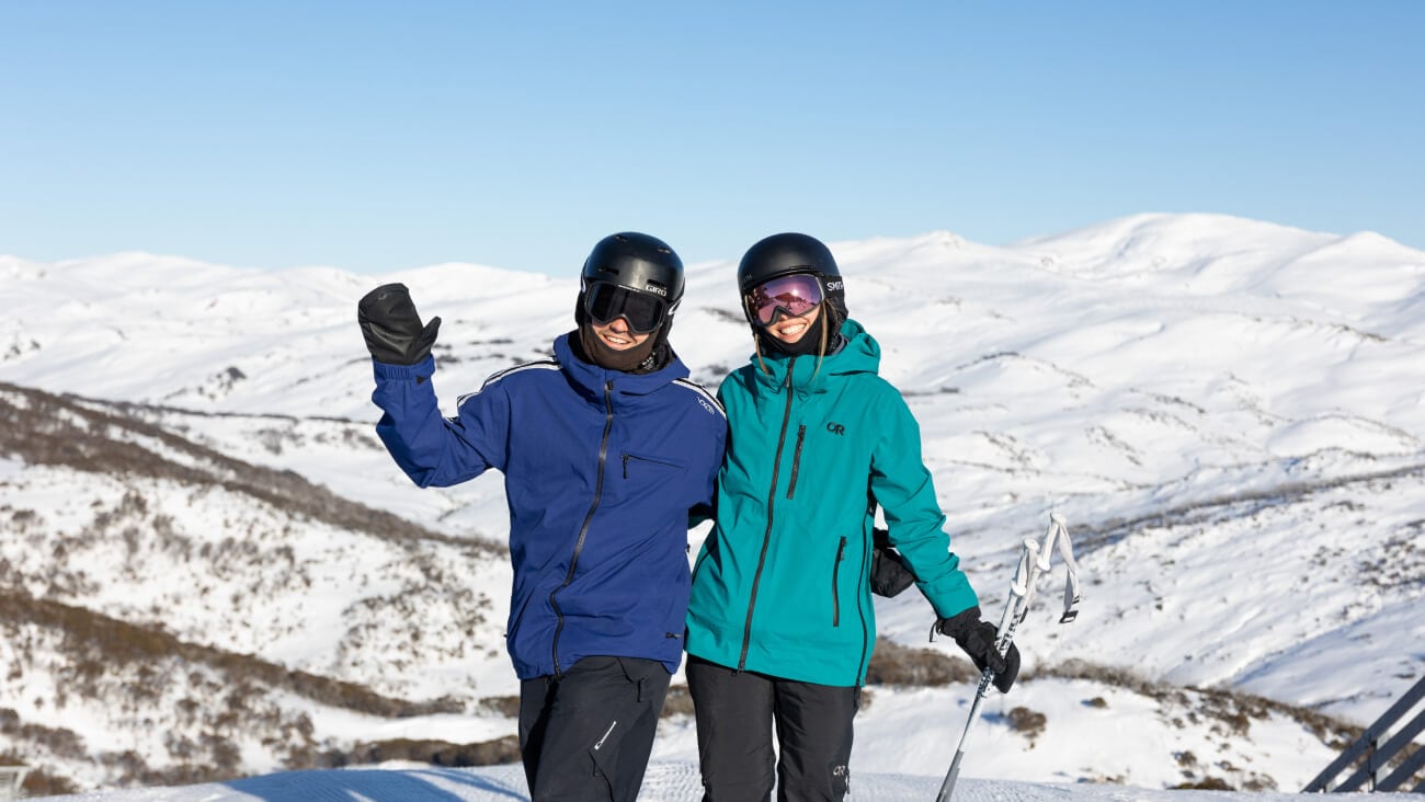 A young man in a blue jacket and young woman in a teal jacket smiling on the Australian ski fields