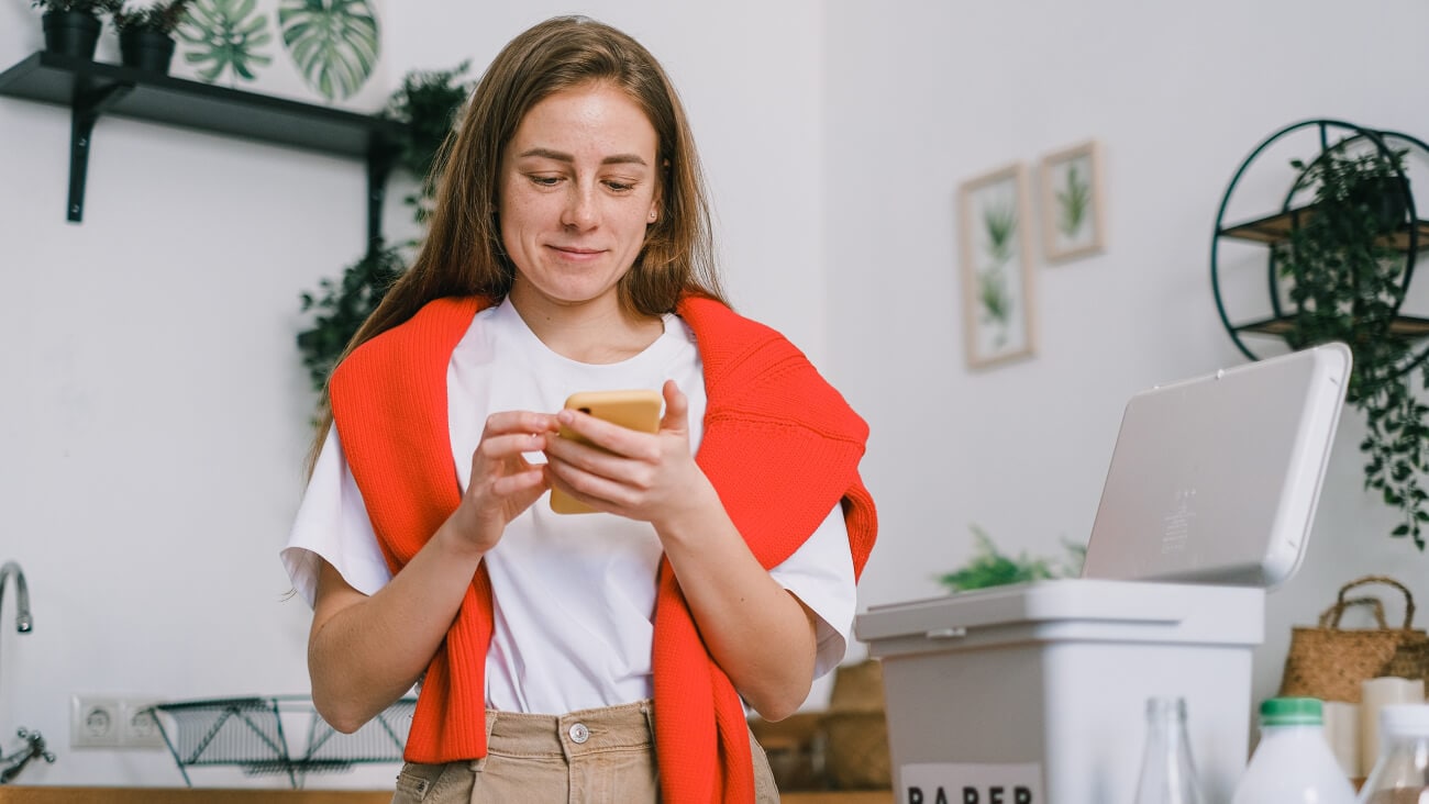 Smiling woman sorting waste and using smartphone