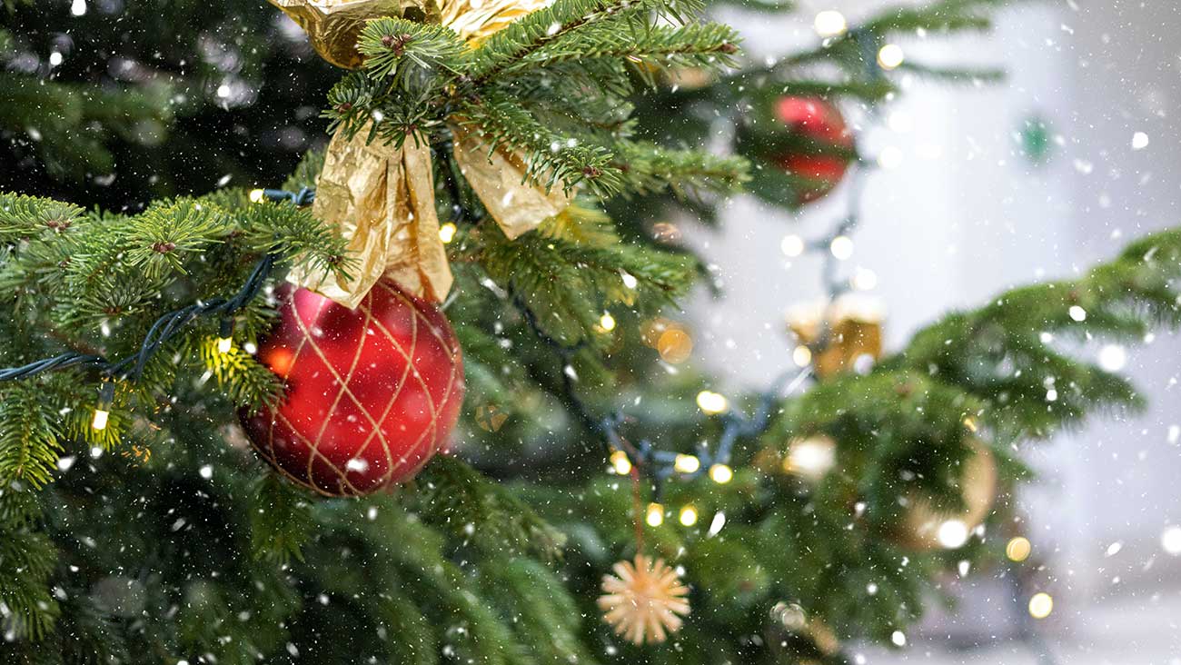 snow falling on decorated Christmas tree with red bauble