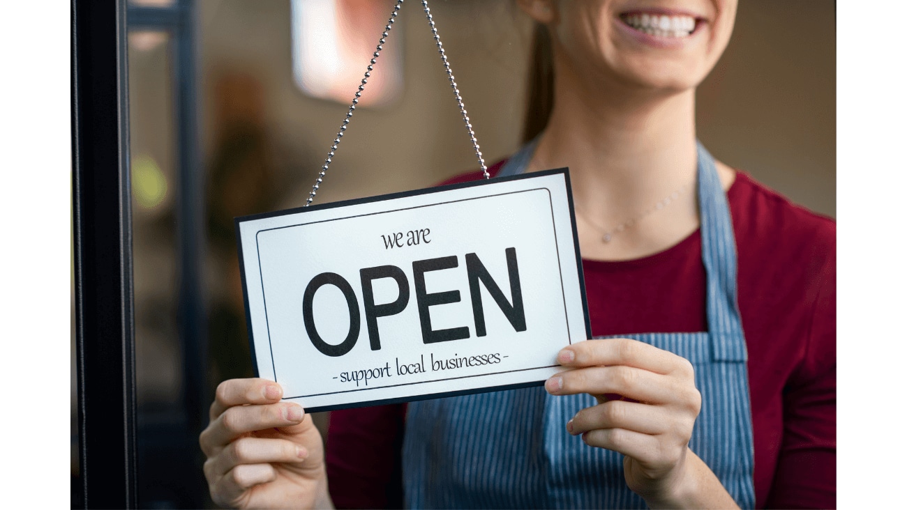 Woman smiling holding a sign reading OPEN