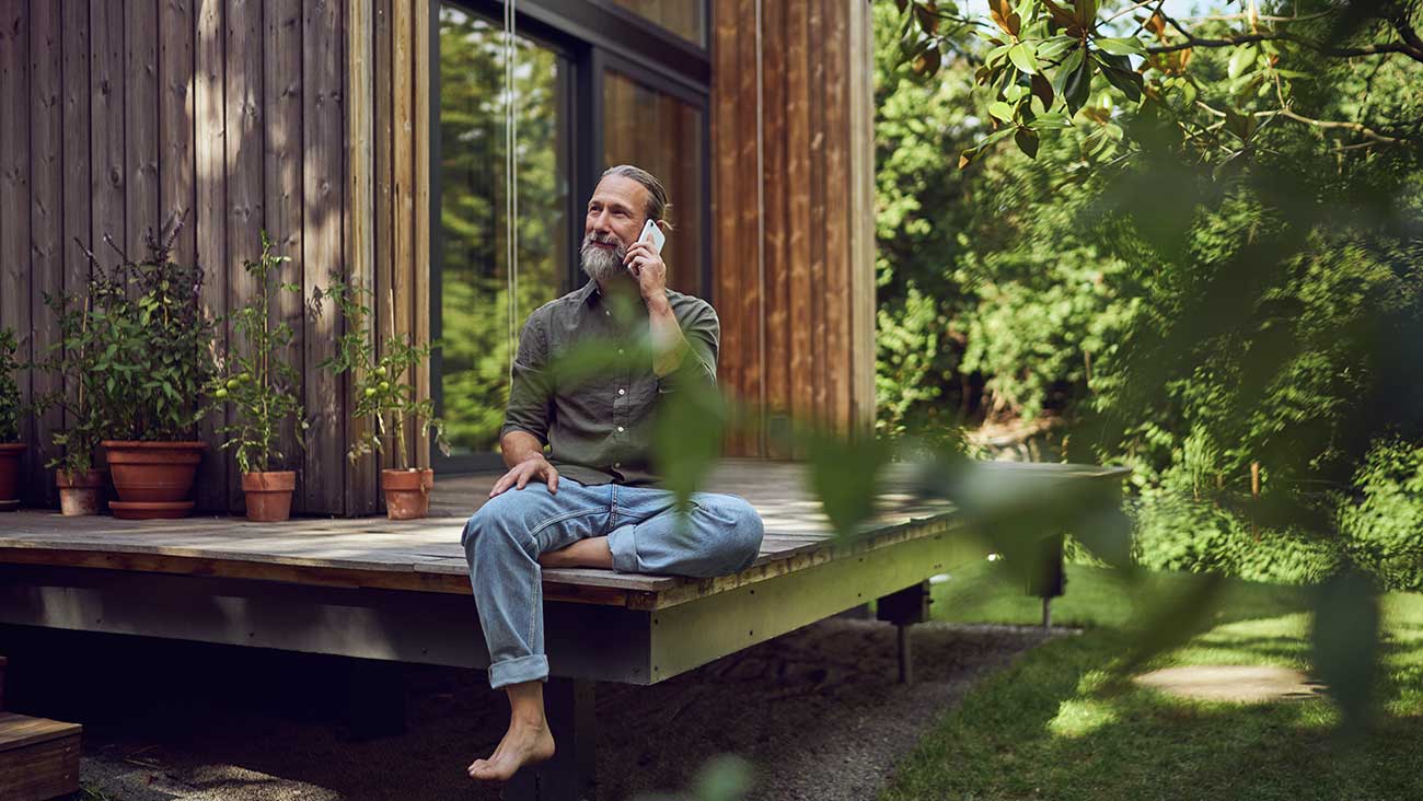 Man sitting outside a cabin in the forest using a mobile phone