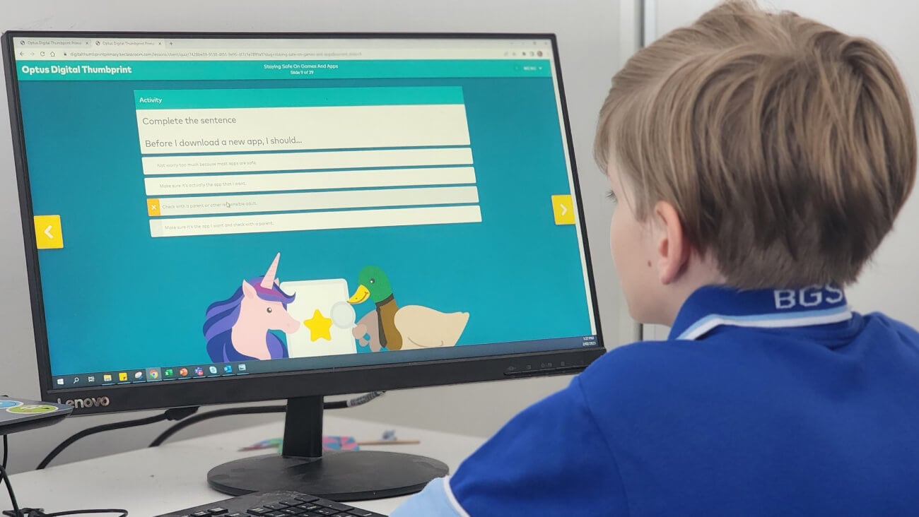 young boy sitting at a computer screen showing a Optus Digital Thumbprint educational program.