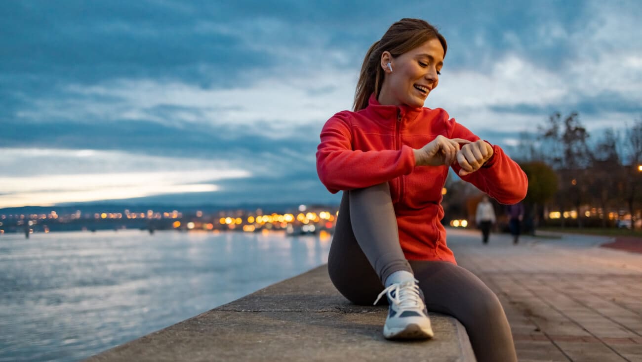 Woman sitting on a bench in sportswear smiling while using a smartwatch