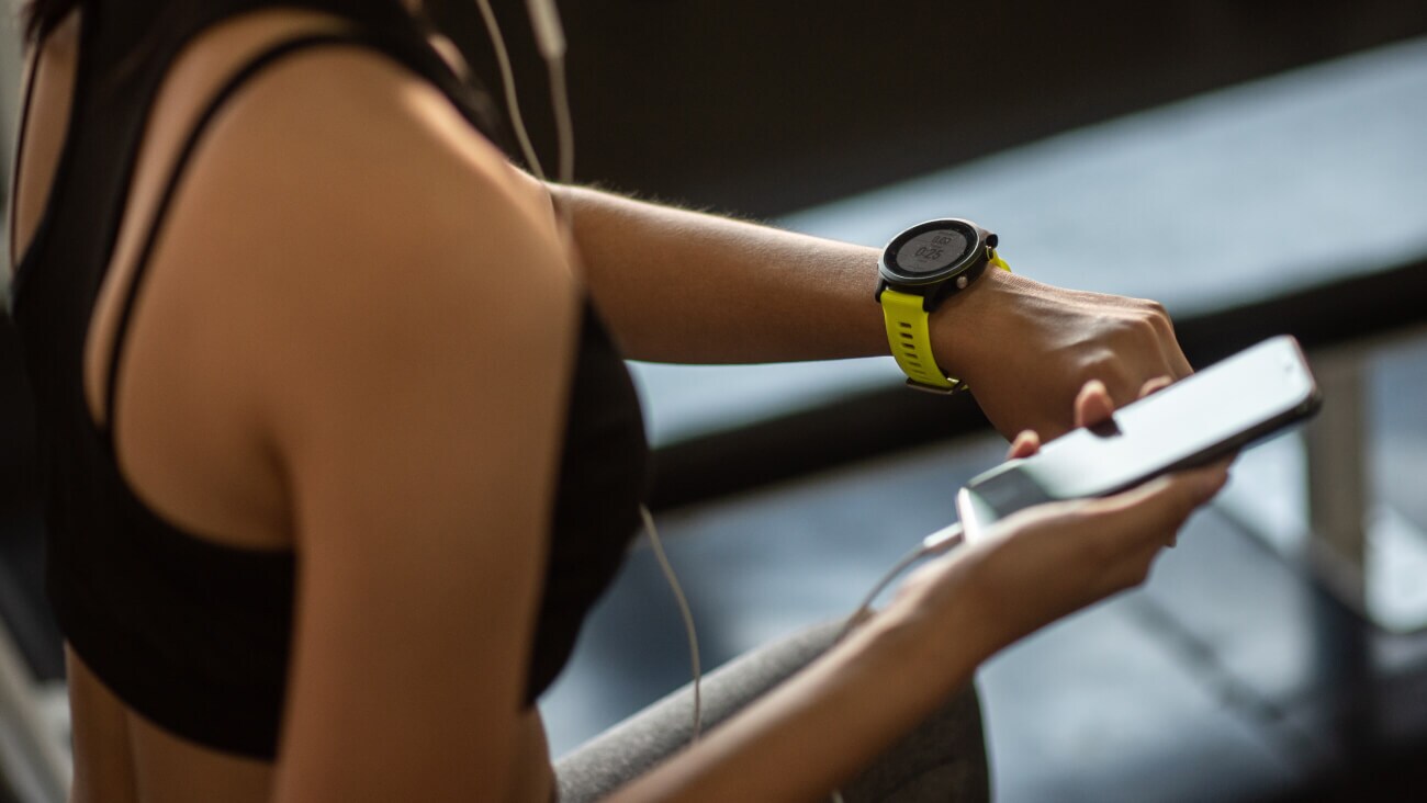 Person wearing a smart watch on one hand and holding a mobile phone on another. The smart watch showing the distance, timer and pace.