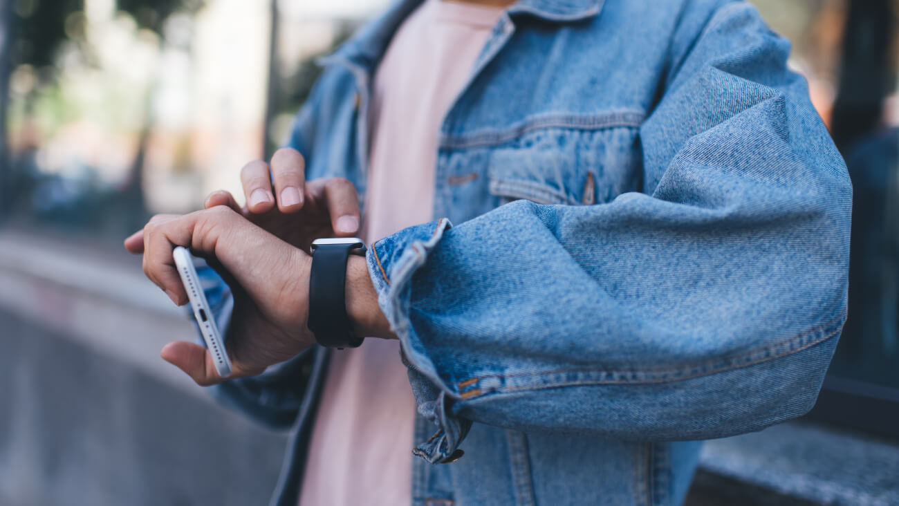 A person wearing a smart watch and holding a mobile phone on one hand and touching the watch screen with his fingers.
