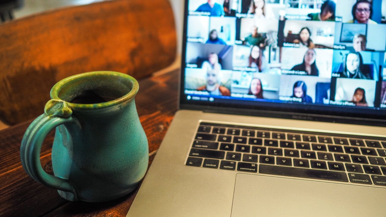 Video conference call with many faces on the screen on a desk with a cup of coffee.