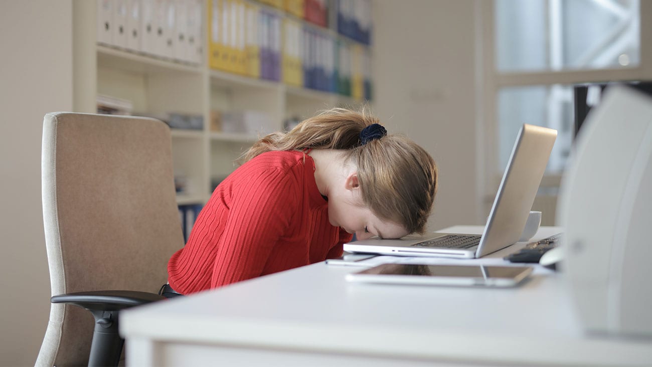 Woman in red top with her head on her down on her laptop