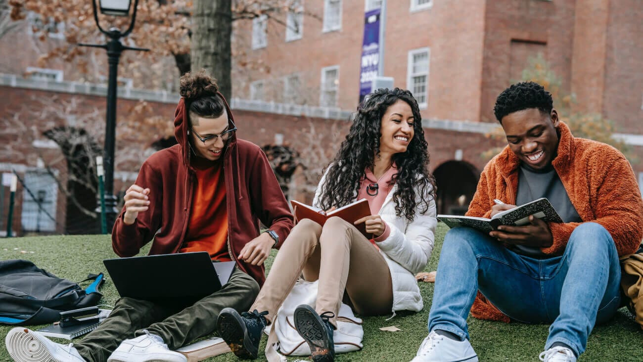 group of cheerful students sitting on campus lawn