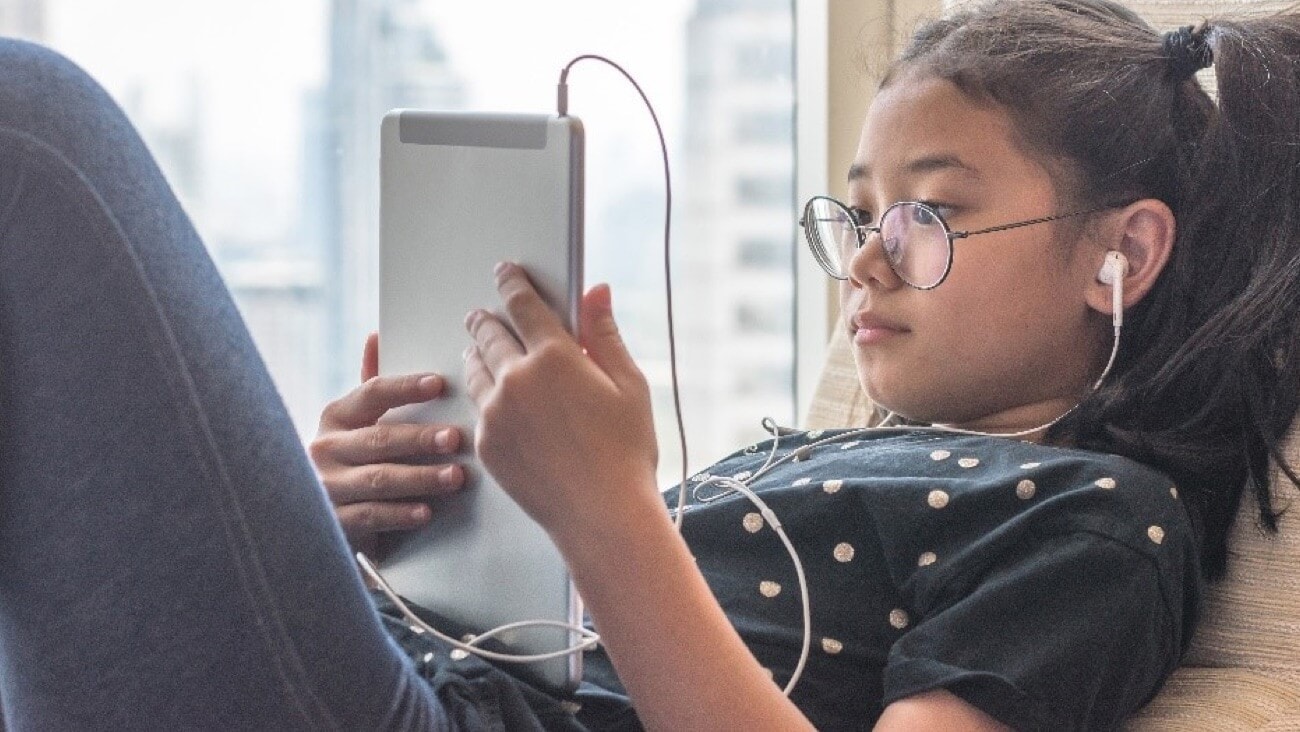 young Asian girl in blue teeshirt using digital computer tablet with earphones