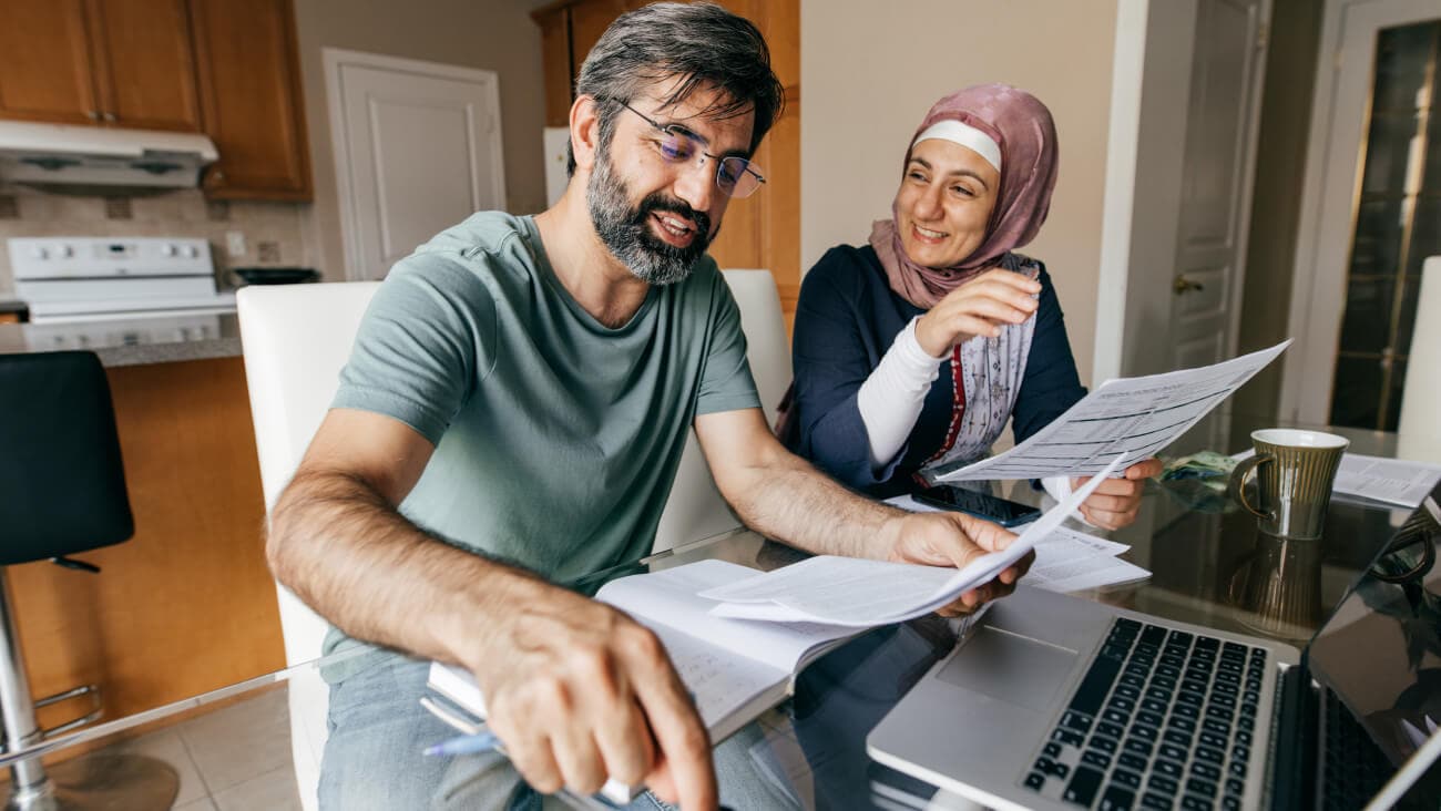 Smiling couple sitting at the kitchen table with paperwork and laptop.