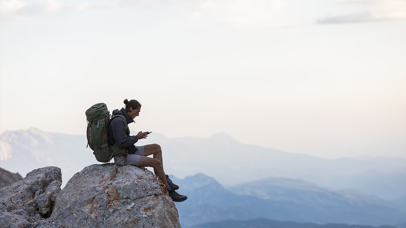 A man sitting on a rock with a backpack looking at his phone