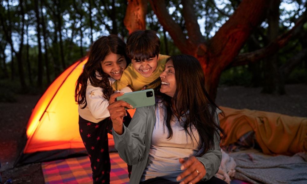 Children and mother on a camping trip sharing a memory on her phone.