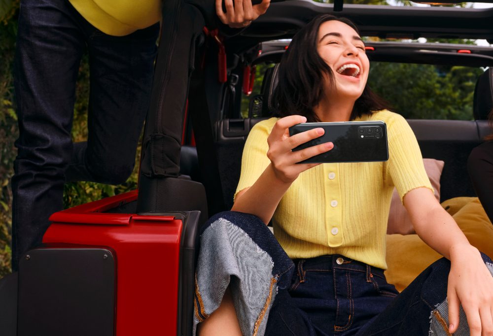 Woman holding an Oppo mobile phone whilst laughing.