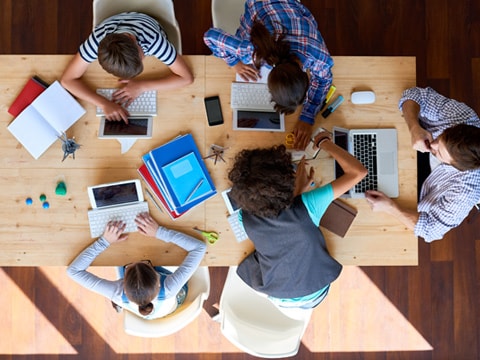 A group of people sitting around a table and using devices