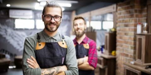 Two smiling men wearing work aprons.