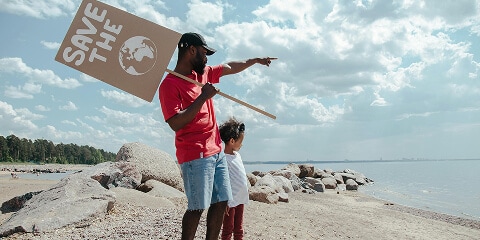 Father holding a sign to save the planet with his child on a beach on Earth Day