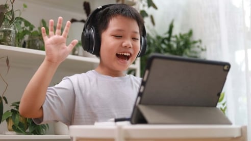 young boy wearing headphones waving to tablet with plants in background