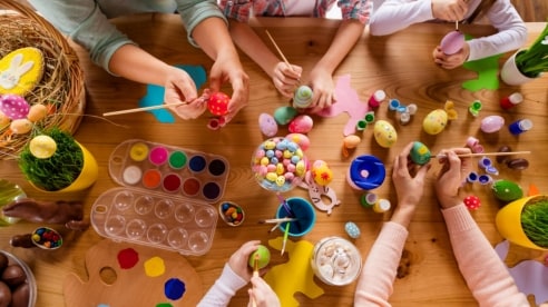 A group of children viewed from above while painting Easter eggs on a wooden table