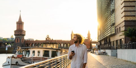 Young many walking with his mobile phone by the river in Berlin.